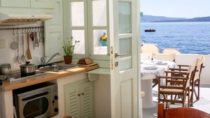 Une cuisine avec vue sur la mer, un coin repas avec des chaises en bois et une table dressée pour deux personnes.