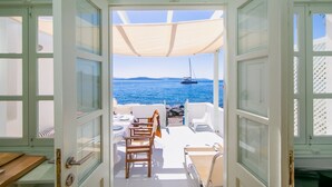 Une porte ouverte donne sur une terrasse où une table est dressée pour le repas, et d’où l’on peut admirer un plan d’eau avec un voilier.
