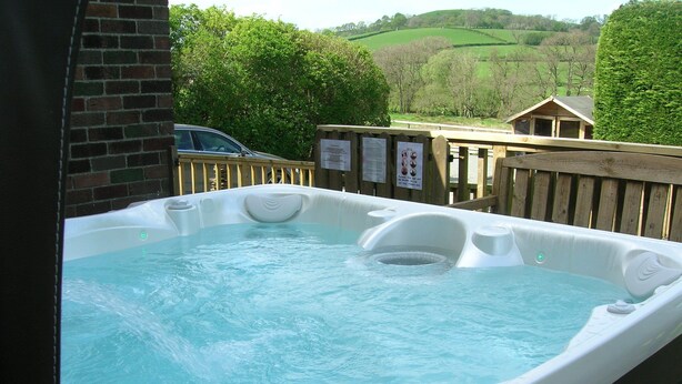 A hot tub with a wooden deck and a view of a green landscape.
