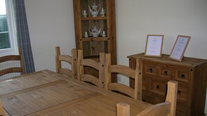A wooden dining table with chairs, a wooden cabinet with drawers, and a window with curtains.