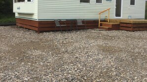 Une maison mobile dotée d’un porche à l’avant, d’une petite terrasse et d’une allée en gravier.