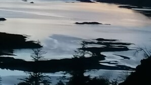 Un paysage côtier avec des eaux calmes, des montagnes lointaines et un ciel dégagé.