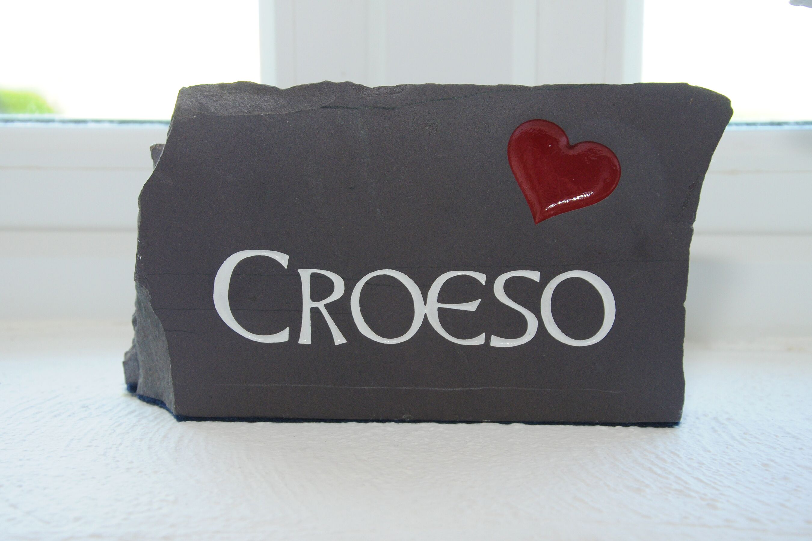 Un objet rectangulaire de couleur sombre, portant le mot « Croeso » et un symbole de cœur rouge.