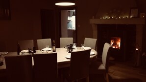 Uma sala de jantar com iluminação suave, lareira, mesa posta para quatro e luminária pendente.