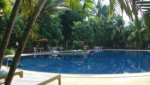 Una piscina rodeada de palmeras y follaje, con sillas de descanso y una pequeña mesa.