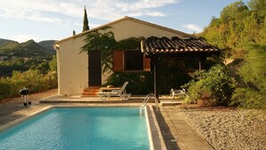 A poolside area with a pool, a small building with a tiled roof, and a view of hills in the background. - Secluded Villa With Private Pool (Lodève)