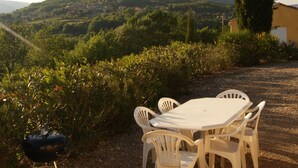 A table and chairs set outdoors with a view of a hilly landscape and a tall tree. - Secluded Villa With Private Pool (Lodève)