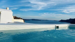 Um edifício branco com piscina que se estende até o mar, sob um céu claro.