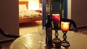 A table with a bottle and candle, a glass, and a chair in a room with a bed and a balcony.