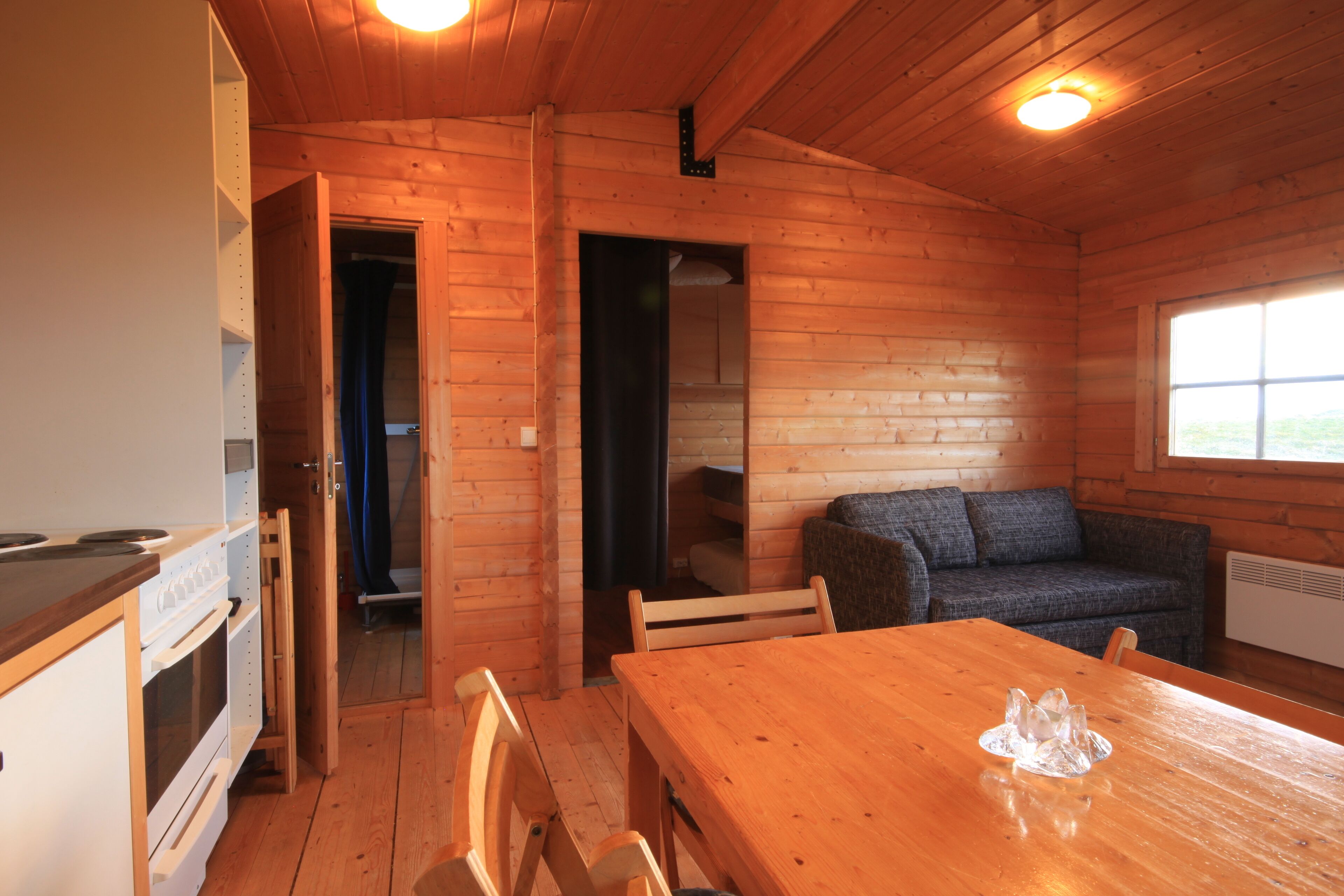 Ein Holzblockbau-Innenraum mit Esstisch, Stühlen, einer Couch und einer Küchenzeile mit Herd und Backofen.