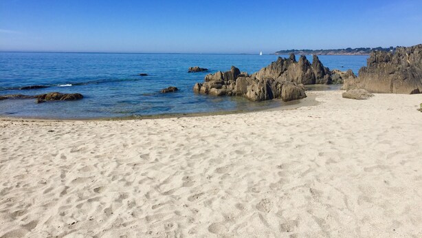 Ein Sandstrand mit Felsen und klarem, blauem Wasser.