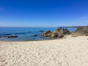 A sandy beach with rocky formations and clear blue water.