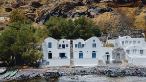 Un bâtiment blanc doté de nombreuses fenêtres et portes, situé près d’une côte rocheuse aux eaux limpides.