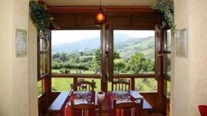 Un espace repas comprenant une table et des chaises, ainsi que de grandes fenêtres donnant sur un paysage verdoyant avec des collines.