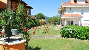 Un jardin avec une balançoire, une fontaine et un sentier menant à un bâtiment doté d’un toit en tuiles.