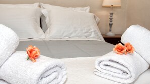 Een net opgemaakt bed met witte lakens en twee handdoeken met oranje bloemen.