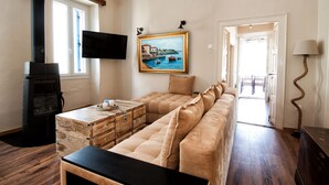 Een gezellige woonkamer met een bank, een houten dressoir, een open haard en een schilderij van een kustlandschap.
