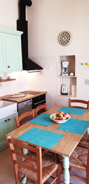 Una cocina con gabinetes color turquesa, una campana extractora negra, una cafetera y un reloj en la pared.