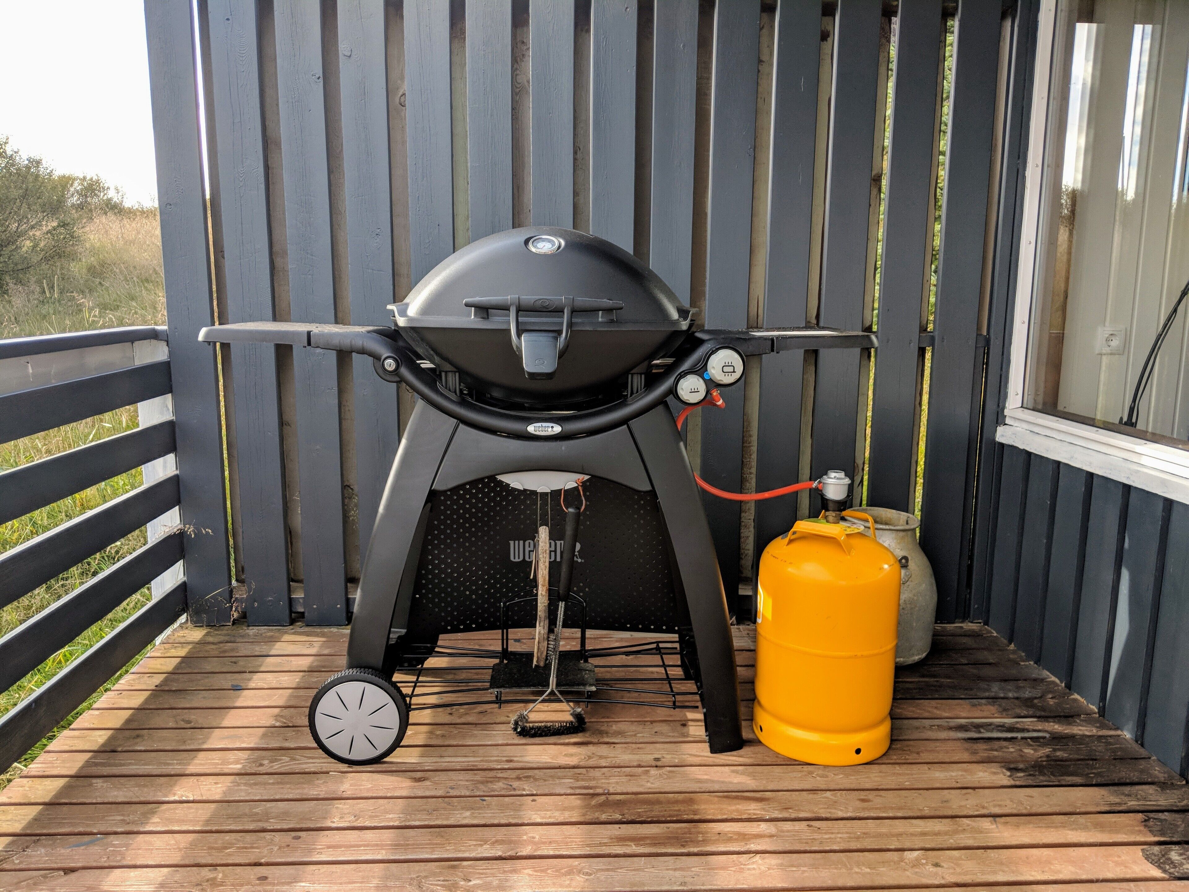 Ein tragbarer Grill mit Gasflasche auf einer Holzterrasse.