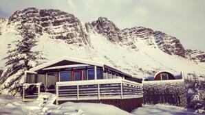 Uma pousada nas montanhas coberta de neve, com fachada de madeira e porta vermelha.