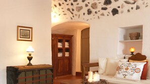 Een gezellige woonkamer met een stenen muur, een houten kast, een lamp, een bank met decoratieve kussens en een klein tafeltje met kaarsen.
