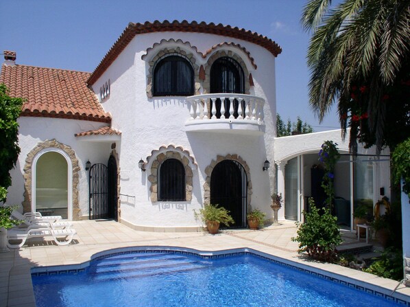 A two-story building with a swimming pool, stone arches, and a tiled roof.