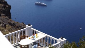 Un balcon avec une table, donnant sur une mer d’un bleu profond, où l’on peut apercevoir deux navires de croisière et un phare.
