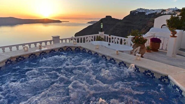 Un bain à remous offrant une vue sur un coucher de soleil se reflétant sur une étendue d’eau et un paysage montagneux.