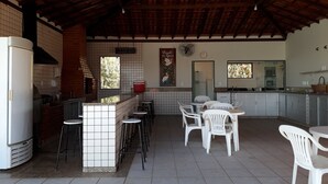 Un'ampia cucina con zoccolo in piastrelle, un forno a mattoni e un frigorifero. Sono presenti sedie in plastica bianca e un tavolo da pranzo.