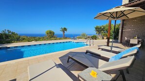 Un espace piscine équipé de chaises longues et d’un parasol, offrant une vue panoramique sur la mer.