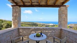 Un espace extérieur aménagé avec des murs en pierre, comprenant une table et des chaises, et offrant une vue sur un paysage côtier.
