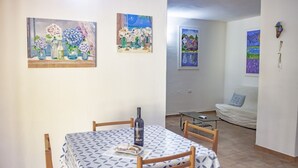 Una zona de menjador amb una taula ben a punt per a dues persones, una ampolla de vi i un quadre amb flors a la paret.