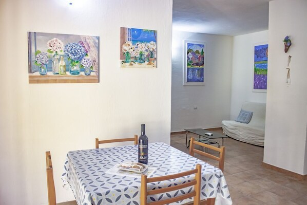 A dining area with a table set for two, a bottle of wine, and a painting of flowers on the wall. - Su Moddissi by All4sardinia (Cardedu)