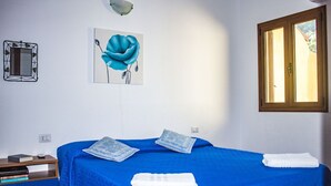 Un dormitori amb un estri de llit blau, un quadre d'una flor blava, una finestra amb una vista i un mirall fixat a la paret.