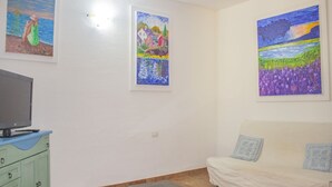 Un saló amb televisió sobre un moble, un sofà i tres quadres a la paret.