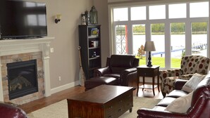 A spacious living room with a fireplace, leather furniture, a television, and large windows offering a view of a dock and water.