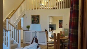 Een ruime woonkamer met een trap, een bank, een eettafel en een kroonluchter.