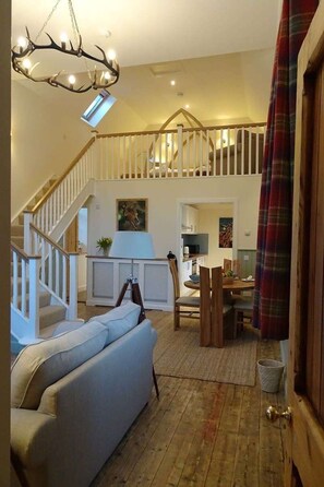 A spacious living area with a staircase, a sofa, a dining table, and a chandelier.