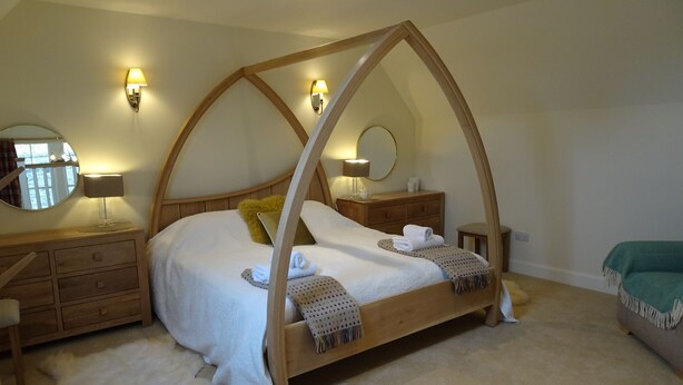 Een slaapkamer met een hemelbed, houten meubels, een ronde spiegel en twee wandlampen.