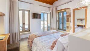 Ein Schlafzimmer mit Bett, Schreibtisch, Stuhl, Fernseher und großen Fenstern.