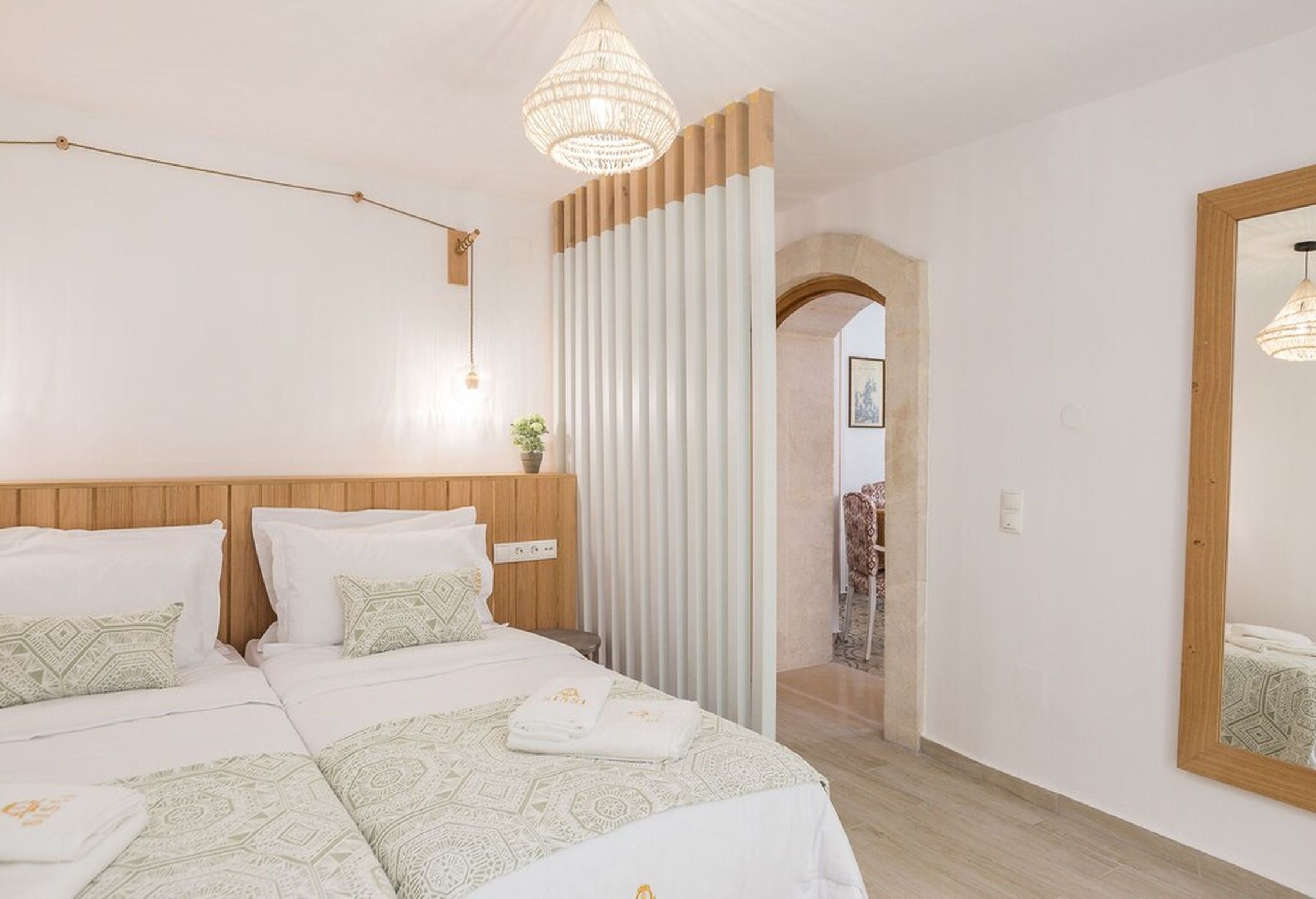A hotel room with a large bed, a wooden headboard, a chandelier, a mirror, and a view of the hallway.