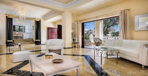 A spacious living area with a white sofa, a glass coffee table, and a chandelier.
