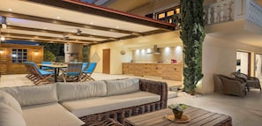 A spacious patio area with a dining table, blue chairs, a wicker sofa, and a kitchen in the background.