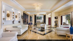 A luxurious living room with a chandelier, white sofas, and a marble floor.