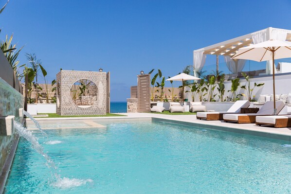 A pool area with a clear view of the ocean, lounge chairs, and a water feature.