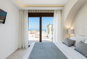 A hotel room with a large bed, a TV mounted on the wall, and a view of the beach and ocean through a sliding door. - Villa Moana - Beachfront Coastal Dreams by etouri (Rethymno)