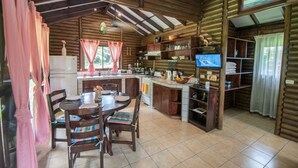 A cozy cabin-style kitchen with wooden walls, a dining area with a table and chairs, and a television on the counter. - Cabaña Los Tucanes - Paradise for Couples! (La Fortuna, Costa Rica)