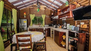 A rustic wooden cabin with a dining area, kitchen, and a TV mounted on the wall. - Cabaña Los Tucanes - Paradise for Couples! (La Fortuna, Costa Rica)