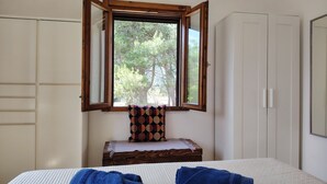 Ein Schlafzimmer mit Bett, Fenster, einer Holzbank und einem Kleiderschrank.