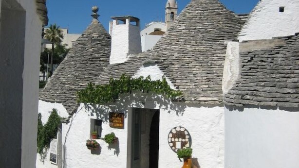 Eine schmale Straße mit traditionellen Gebäuden mit Stein-Dachziegeln, blauem Himmel und einer großen Vase im Vordergrund.